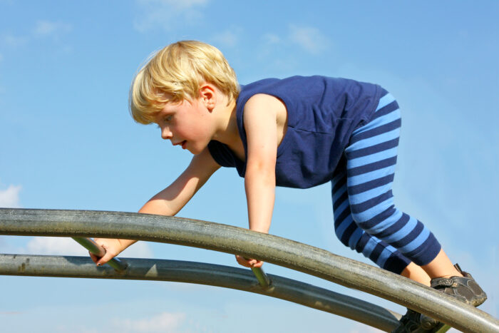 A cute little boy is carefully climbing a ladder toy at the playground on a summer day