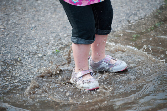 toddler standing in a puddle with water shoes on