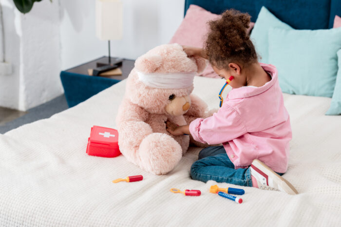 Little girl in pink playing doctor with teddy bear